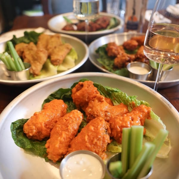 Plates of buffalo wings with celery sticks and dipping sauce, with wine glasses on a table.