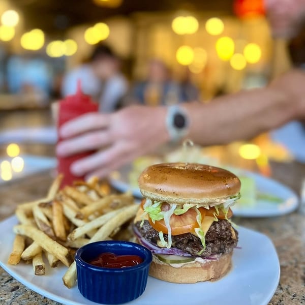 A double cheeseburger with lettuce, tomato, and onion, served with fries and ketchup on a white plate.