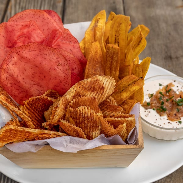 A wooden box filled with red, yellow, and waffle-cut chips, served with a side of dip.