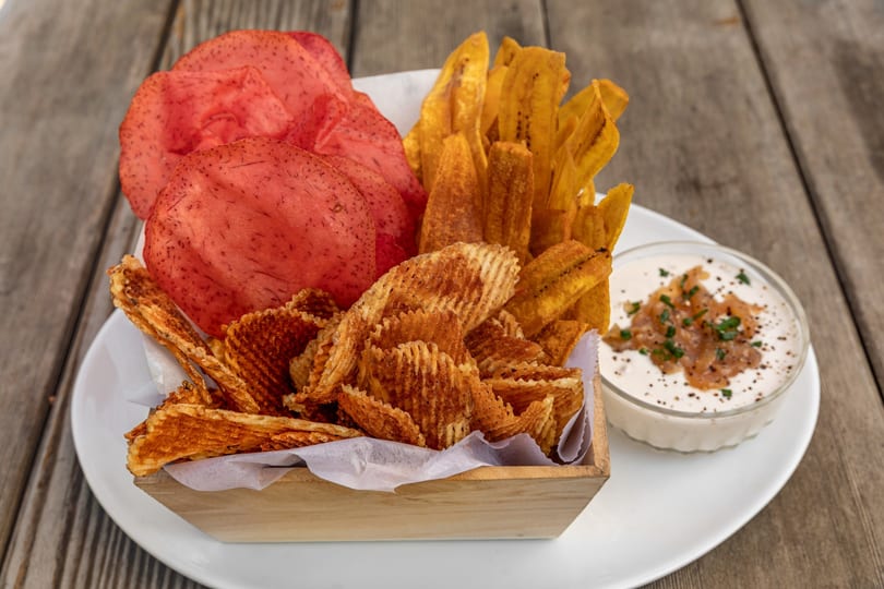 A wooden box filled with red, yellow, and waffle-cut chips, served with a side of dip.