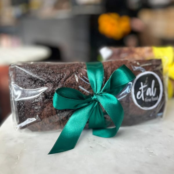 Chocolate loaf cake wrapped in plastic with a green ribbon and an "et al fine food" sticker.